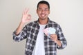 Adult asian man smiling happy giving Ã¢â¬ÅOKÃ¢â¬Â sign while holding paper money